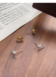 Detailed view of silver and gold bow stud earrings on a textured wooden background