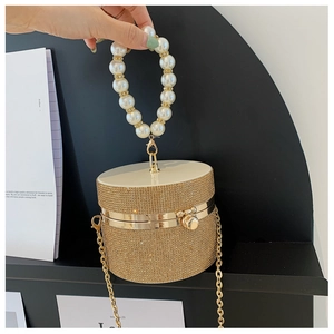 Detail of a gold cylinder clutch bag with champagne rhinestones and large pearl handle