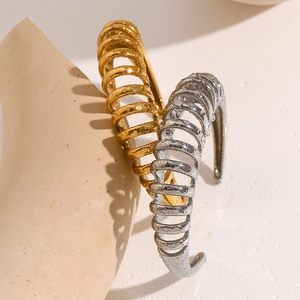 Detailed shot of 18K gold and silver spiral wave bangles with water droplets on stone