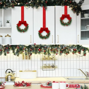 Mini Christmas wreaths with red bows hanging on white kitchen cabinets by red ribbons