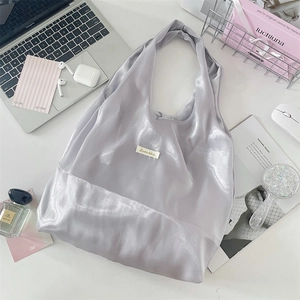 Flat lay of a silver satin tote bag with metallic texture next to a laptop and perfume