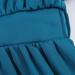 Gros plan sur la texture satinée plissée et le design smocké d'une robe mi-longue bleu sarcelle