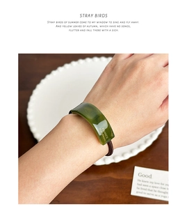 Detail showing green acetate hair tie with engraved gold plaque and elastic cord