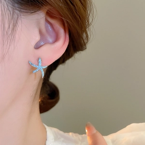 Primo piano di orecchini a lobo stella marina blu con perni in argento su modella