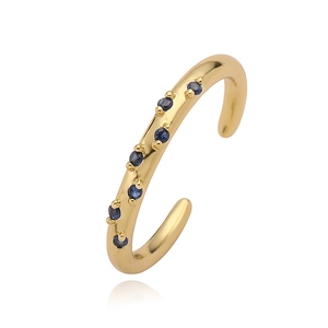 Crossed golden open ring with round blue sapphires and polished finish on white background