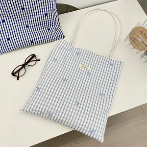 Detail of blue plaid tote bag featuring delicate bow embroidery and brand logo