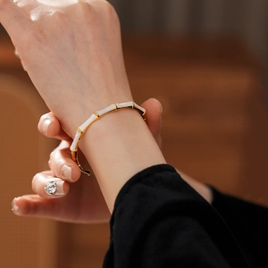 Detail of gold-plated bamboo-style bracelet with white enamel on a female wrist