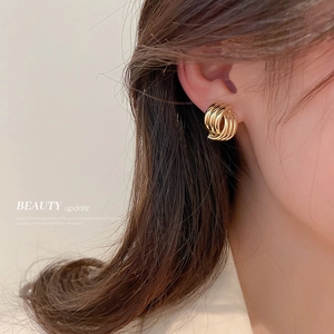 Modern intertwined geometric knot stud earrings in shiny gold finish on female model