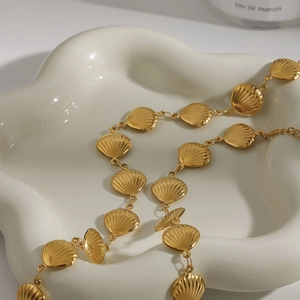 Détail d'un collier chaîne en forme de coquillage doré sur un plateau en céramique