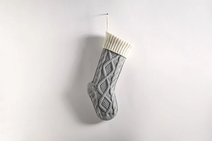 Detail of grey knitted Christmas stocking with white cuff and texture on white wall