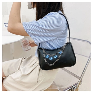 Detail of black shoulder bag featuring silver chain and blue butterfly pendants