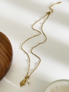 Detail of gold necklace with conch pendant and baroque pearl on white surface