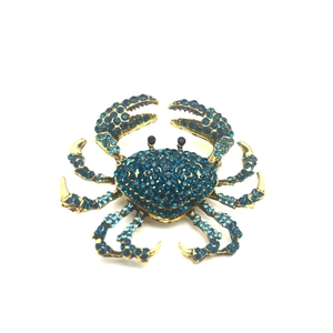 Golden crab brooch featuring deep blue rhinestones on a white background