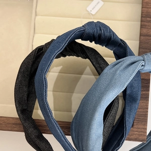 Detailed view of three knotted denim headbands in black, navy, and light blue on a wooden tray