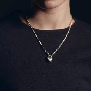 Close-up of silver heart pendant with thick rope chain on model with dark background