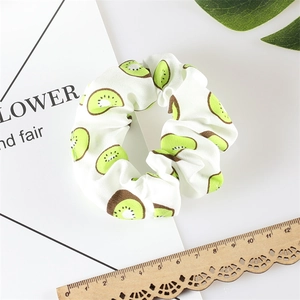 Detailed flat lay of white hair scrunchie with green kiwi fruit print and vintage ruler