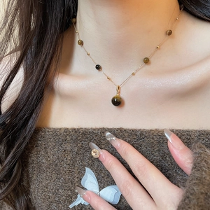 Close-up of a tiger eye stone pendant necklace on a gold chain worn by a model