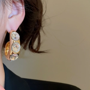 Makroaufnahme großer goldener C-förmiger Ohrringe mit weißen Kristallen am Model