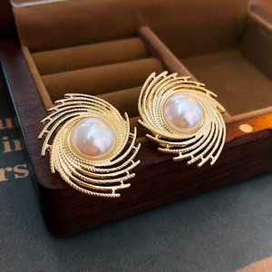 Detail of vintage whirlpool gold pearl earring on a dark brown wooden jewelry box