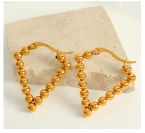 Detail of golden geometric triangle earrings made of small metal beads on a beige stone