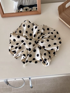 Polka dot satin scrunchie with white pearl accents shown in a warm home setting