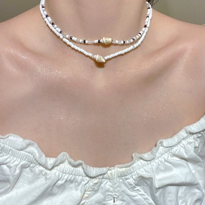 Gros plan sur un collier bohème double couche en perles blanches et pendentifs coquillages
