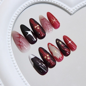 Deep red and black stiletto press-on nails with stars and flame patterns on mirror tray