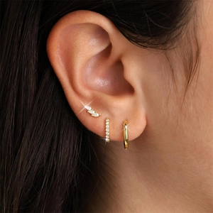 Detail of three gold earrings with zircons worn on model ear for elegant style