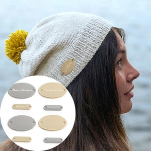 Detail of custom metal tags for knit hats in gold and silver finishes with pre-drilled holes