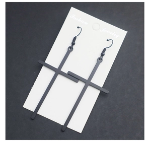 Macro detail of long black matte metal cross earrings on white fashion jewelry card
