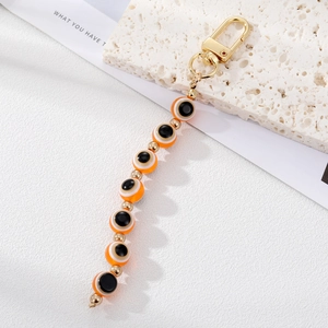 Detailed view of orange Evil Eye beaded keychain with gold charms on a stone surface
