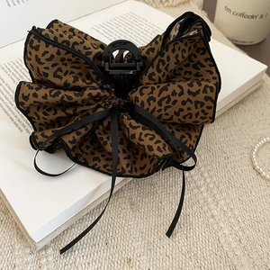 Detailed view of leopard print bow hair claw with lace edges and black ribbons on a book