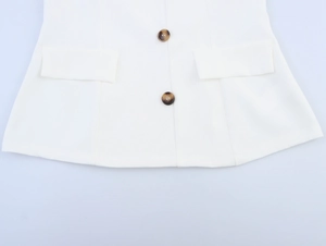Detailed view of white vest featuring amber buttons and symmetrical pocket flaps