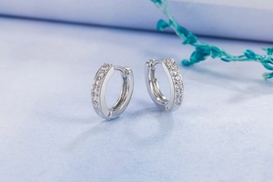 Close-up of silver hoop earrings with a row of sparkling crystals on a textured blue surface