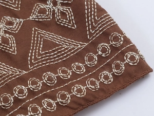 Gros plan sur la broderie ethnique et la texture du tissu marron d'une robe longue