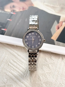 Detailed view of women's silver metal strap watch with dark grey rhinestone dial on a magazine