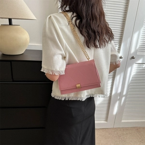 Pink quilted crossbody bag with gold chain strap shown on model in a cozy interior