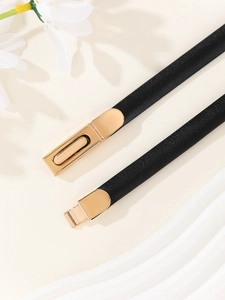 Macro shot of minimalist black patent leather skinny belt with a gold metal buckle