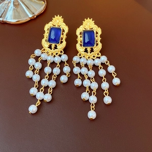 Detail of vintage gold earrings with blue gemstone and white pearl tassels on brown background