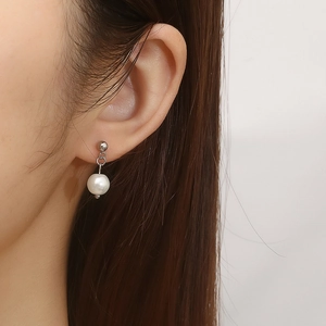 Detail of silver stainless steel C-shape earring with pearl pendant on model ear