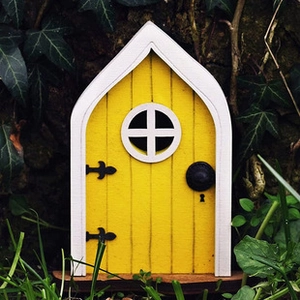Close-up of a miniature yellow wooden fairy door with a white arch in a lush green garden