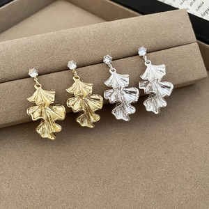 Close-up of gold and silver ginkgo leaf earrings with zircon on a velvet stand