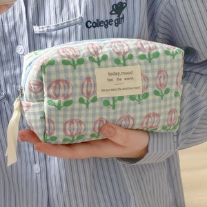 Blue plaid makeup bag with pink tulip patterns held in a casual lifestyle setting