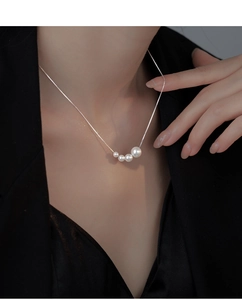 Detail view of four graduated white pearls on a slim silver chain worn with a suit