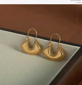 Macro detail of gold-plated fan-shaped earrings with fine beaded edge on jewelry box