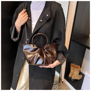 Detail of dark brown ruched cloud bag in glossy patent leather with shoulder strap