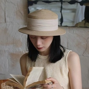 Detail of khaki straw sun hat with wide ivory pleated ribbon band on a model reading