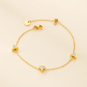 Detail of gold triangle bracelet with pavé cubic zirconia on soft beige background
