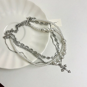 Detail of multi-layer necklace with white pearls and black stone cross pendant on ceramic