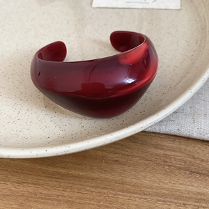 Detail view of a thick dark red acrylic open cuff bracelet on a ceramic tray